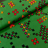 A close-up of a green patterned fabric with a geometric design featuring black, red, orange, and pink diamond and square motifs.