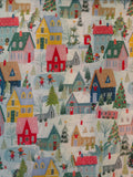 A close-up of a Christmas-themed fabric pattern featuring colorful houses, snowy ground, trees, and small figures in winter clothing.