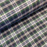 A close-up of a plaid fabric with a green, navy, and white tartan pattern, showing a rolled section on top of the flat fabric.