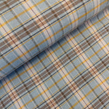 A close-up of plaid fabric with a light blue base, overlaid with brown, beige, and yellow stripes.