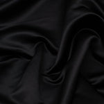 Duchess Satin fabric is a highly lustrous, smooth, very finely woven heavy non stretch satin. It has a very subtle sheen that is classic and elegant and very different in appearance to most satins which generally have a high gloss finish. This is the classic rich black. Sold in half meter lengths at Fabric Focus.