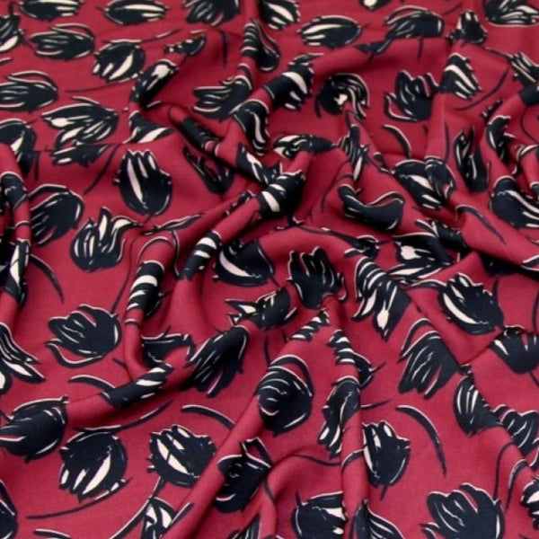 This soft and drapey polyester crepe fabric is a medium weight and is completely opaque, so perfect for sewing tops, skirts, dresses, trousers and jumpsuits. Wine background with tulip like floral motif. Available to buy in half metre increments at Fabric Focus.