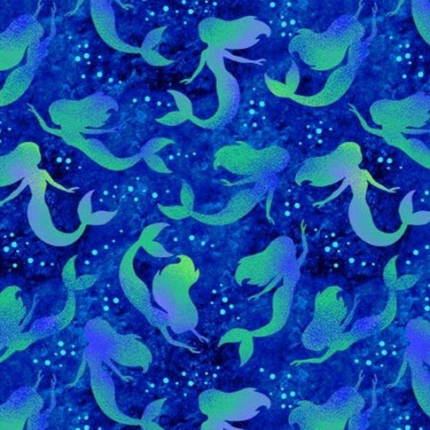 Beautiful silhouettes of long haired mermaids in shades of green and purple on a dark blue sea background. Available to buy in quarter metre increments at Fabric Focus Edinburgh